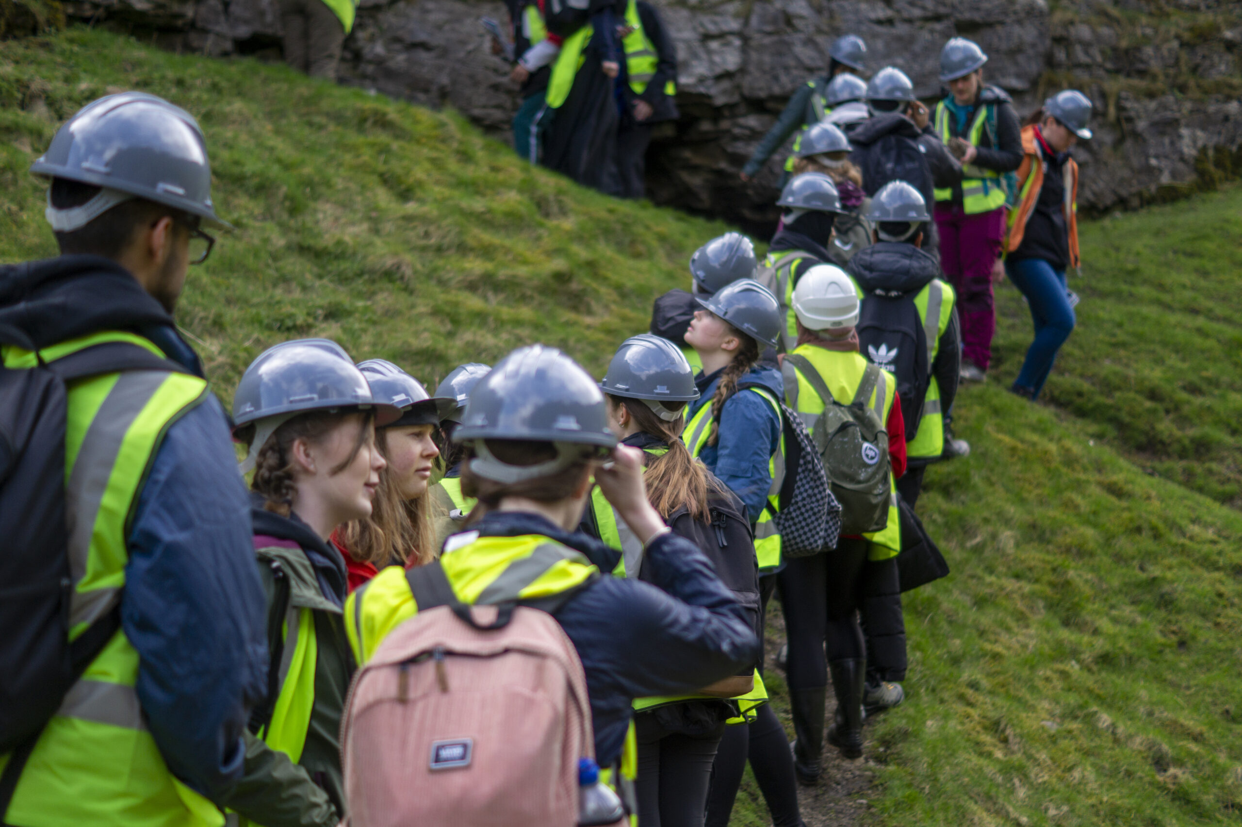 Queue of spring school participants in hard hats and high vis vests in a field. 